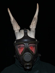 A scary man with glowing red eyes and horns peers through a gas mask, his gaze piercing the darkness with malevolent intent.