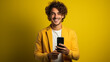© Nadzeya - Curly-haired man in a yellow suit holding a phone and smiling at the camera on a yellow background