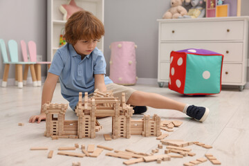 Wall Mural - Little boy playing with wooden construction set on floor in room. Child's toy