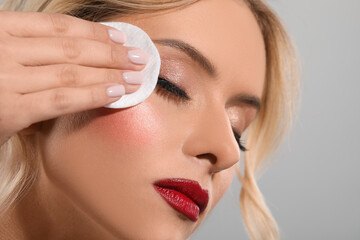 Wall Mural - Beautiful woman removing makeup with cotton pad on light grey background, closeup