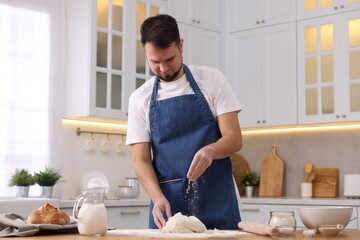 Making bread. Man sprinkling flour onto dough at wooden table in kitchen