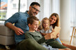 © NDABCREATIVITY - Happy young family having fun time at home. Parents with children using tablet