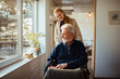 © Davor - Young woman caring for elderly man in a sunlit room with winter scenery outside
