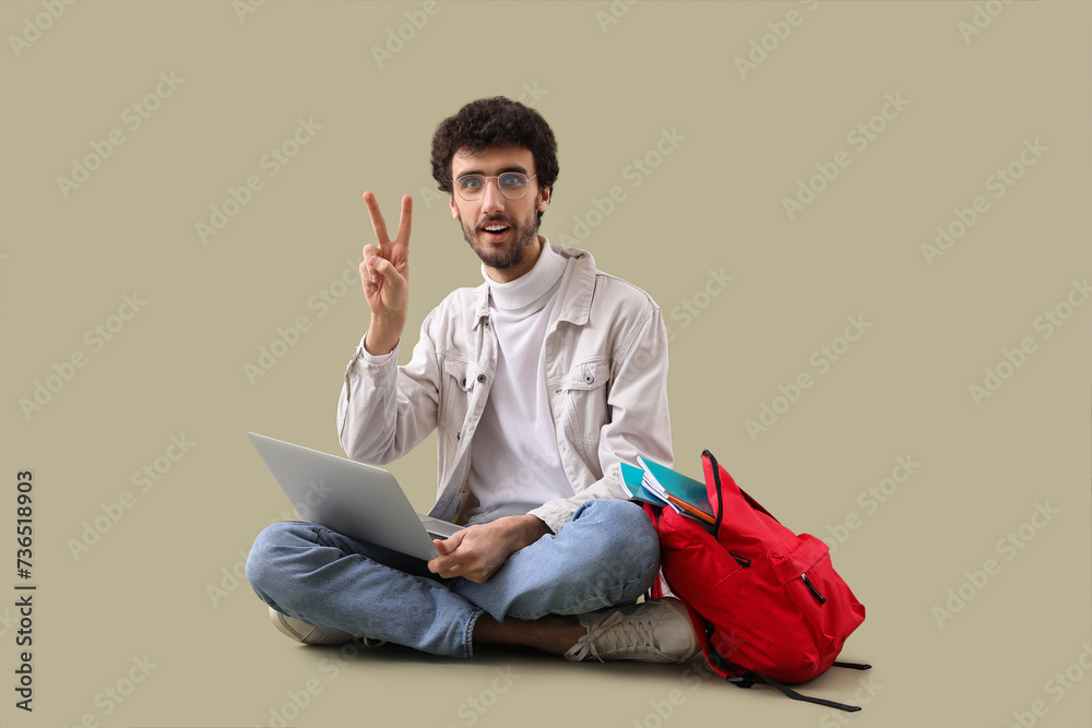 Male student with laptop showing victory gesture on green background