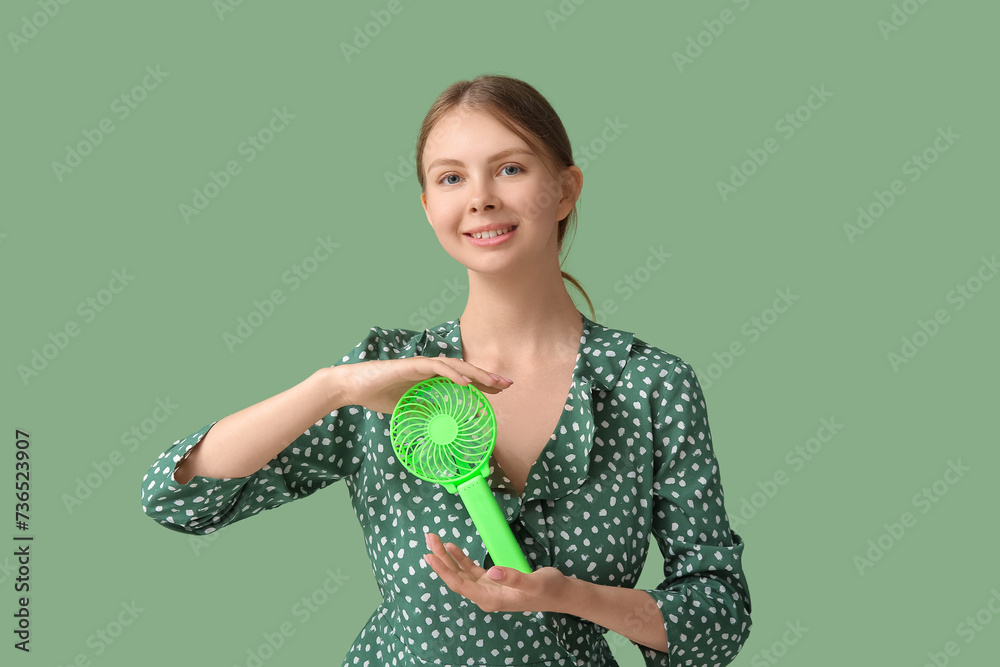 Beautiful young woman with handheld mini fan on green background