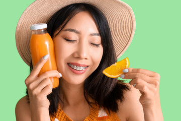 Sticker - Beautiful Asian woman with bottle of juice and orange on green background, closeup