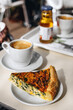 A piece of quiche, french tart consisting of pastry crust filled with eggs and spinach, and some coffee.
