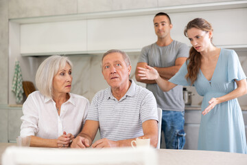 Wall Mural - Couple of adult years man and woman sit in kitchen and quarrel with children