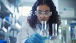 Focused female scientist with curly hair conducts an experiment in a lab, analyzing test tubes with a meticulous gaze behind safety goggles