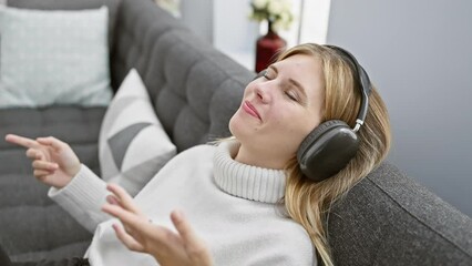 Poster - A contented woman enjoys music with headphones while relaxing on a couch in a cozy living room.