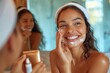 A happy woman smiles as she applies a facial skincare product, looking at her mirror image with satisfaction
