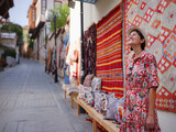 Fototapeta Młodzieżowe - female summer travel to Antalya, Turkey. young asian woman in red dress walk through old town Kalechi , female tourist traveler discover interesting places and popular tourist traditional carpet