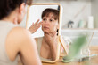 © JackF - Casual focused woman in forties carefully inspecting facial skin in mirror during daily beauty regimen at home