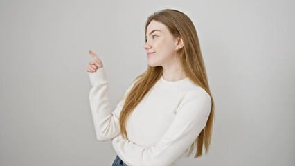 Canvas Print - Young, happy blonde woman smiling joyfully, confidently pointing to the side with her finger while standing against an isolated white background, wearing her cozy sweater.