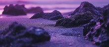 A Cluster Of Rocks Resting On A Sandy Beach With Purple Hues, Surrounded By Water. The Natural Landscape Is Complemented By Violet Tones In The Sky At Dusk