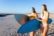 Caucasian young female friends holding surfboards on a sunny beach
