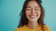 © Z A C - Smiling young woman with glasses closed eyes and wavy hair wearing a yellow top against a light blue background.
