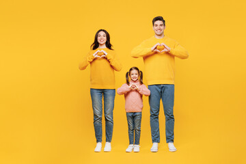 Wall Mural - Full body young happy parents mom dad with child kid girl 7-8 years old wear pink casual clothes showing shape heart with hands heart-shape sign isolated on plain yellow background Family day concept