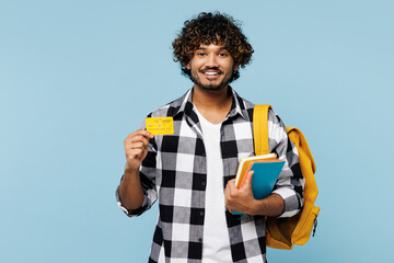 Wall Mural - Young smiling Indian boy student wear shirt casual clothes backpack bag hold mock up of books credit bank card isolated on plain pastel light blue background. High school university college concept.