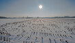 Pokryte śniegiem pole ściętej kukurydzy w mgliste styczniowe popołudnie.Przedmieścia Ostrowca o rolniczym charakterze w wczesne zimowe popołudnie. Słońce świeci przez chmurę mgły na niebie.