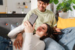 © Studio Marmellata - Playful and affectionate interaction as a man shares his smartphone screen with a smiling woman, intimate moment on a couch