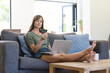 © Wavebreak Media - A middle-aged Caucasian woman is comfortably seated on a sofa, holding a credit card while looking a
