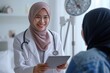 Smiling Asian female doctor in hijab showing digital tablet screen to patient, explaining examination results, medical examination, giving consultation at appointment