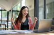 © Wasana - Cheerful young Asian woman with braces enjoying a triumphant moment at her office desk with a laptop..