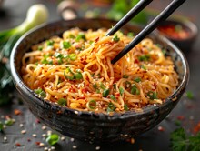 A Bowl Of Noodles With Chili-garlic Oil. The Bowl Contains Wide, Flat Noodles Coated In A Glistening, Spicy Garlic Oil, With Noticeable Flecks Of Red Chili Flakes And Crushed Garlic.