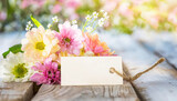 Fototapeta Tęcza - Colorful spring flowers on rustic light wooden planks with an empty tag for text. Celebration concept