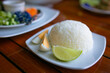 Rice in white plate with sliced lime and egg on wooden table