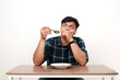 © ArvStd - Young asian man imagining something while holding a spoon with empty plate on the table