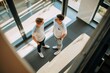 © sambath - High-Angle Shot of Two colleagues talking in a bright office, wearing t-shirts