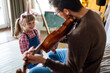 Music is so much fun. Young father teaching his little daughter to play violin and smiling.