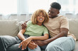 cheerful black man embracing happy girlfriend in braces while sitting on cozy couch in living room