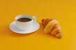 a cup of coffee and croissant on yellow background in