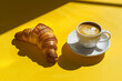 a cup of coffee stands next to a croissant on a yello