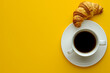 a cup of coffee with a croissant on yellow background