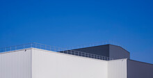 Modern White And Black Aluminium Corrugated Factory Buildings With Steel Fence On Rooftop Against Blue Sky Background In Panoramic View