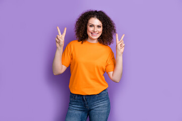 Wall Mural - Photo of cute positive woman wear orange t-shirt smiling showing two v-signs isolated purple color background