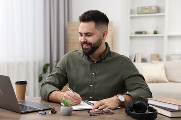 Poster - E-learning. Young man taking notes during online lesson at wooden table indoors