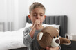 Sick boy with teddy bear coughing at home