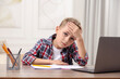 © New Africa - Little boy suffering from headache at wooden desk indoors