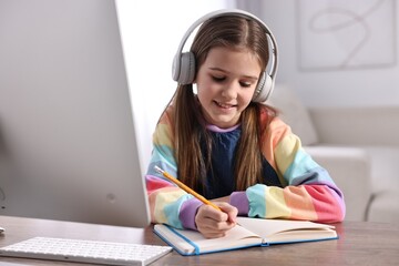 Poster - E-learning. Cute girl taking notes during online lesson at table indoors