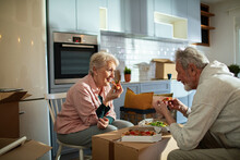 Senior Couple Eating Pizza In New Kitchen With Moving Boxes Around Them