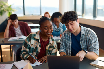 Wall Mural - Happy multiracial students e-learning on laptop while studying in classroom at university.