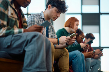 Wall Mural - Young student and his college friends using their cell phone at campus.