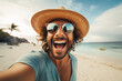 Happy young man with sunglasses and summer straw hat taking selfie at beach