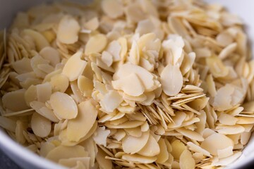 A delicious food close up portrait of a white bowl full of almond flakes used by a baker to create tasty cookies or pastries. The chopped up crunchy cooking and baking ingredient is ready to be used.