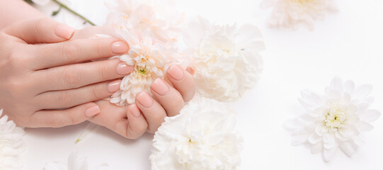 Wall Mural - Concept cosmetic cream and beauty health care. Stylish trendy nail young woman hands pink manicure on white background with flowers, top view